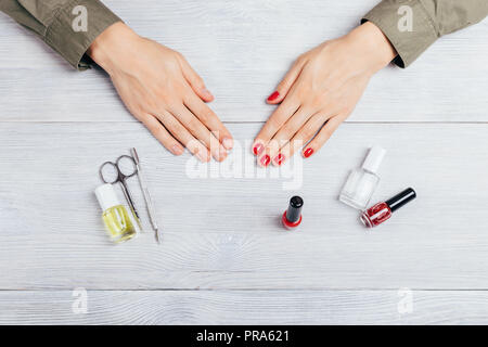Zwei weibliche Hände bei der Maniküre zeigt vor und nach, close-up. Junge Frau angewandten Roten polnischen auf die Nägel neben Tools, Flaschen mit Glitter lacqu Stockfoto