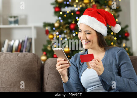 Frau buting auf Linie mit Telefon und Kreditkarte in Weihnachten auf einer Couch im Wohnzimmer zu Hause sitzen Stockfoto