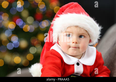 Nachdenklich Baby Tragen santa claus Kostüm auf einer Couch zu Hause in Weihnachten Stockfoto