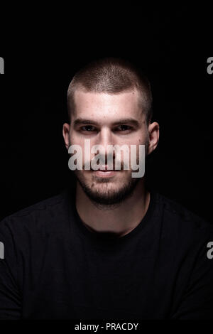 Ein junger Mann, dramatische Portrait. schwarzer Hintergrund. Kopf und Schultern geschossen. Bei camera suchen, schwarzer Hintergrund Studio. Stockfoto