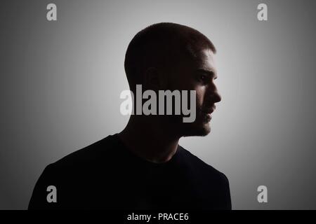 Ein junger Mann, 20-25 Jahre, Moody dunklen Portrait, Profil. studio Shot, grauen Hintergrund. Kopf und Schultern geschossen. Stockfoto