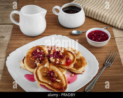 Auf einem weißen Porzellanteller liegen rosy Pfannkuchen mit Johannisbeere Konfitüre gefüllt und mit Nüssen bestreut Stockfoto