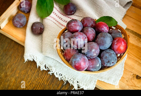 Auf der Tabelle auf eine Serviette Weidenkorb mit Reifen große Pflaumen gefüllt. Stockfoto