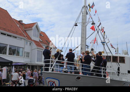 Musiker auf dem Deck eines Schiffes in den Hafen von Bergen, Norwegen, und Menschen, die während der traditionellen Markt Tag (Torgdagen) Festival unterhalten. Stockfoto