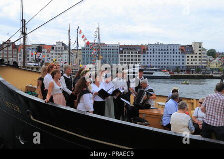 Ein Chor führt traditionelle norwegische Lieder und Volksmusik auf dem Deck eines Schiffes in den Hafen von Bergen, Norwegen, während der Markt Tag (Torgdagen). Stockfoto