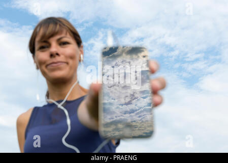 Glückliche Frau Musik zu hören und Ihre Smart Phone Reflex der Himmel mit Wolken in der Schweiz. Stockfoto