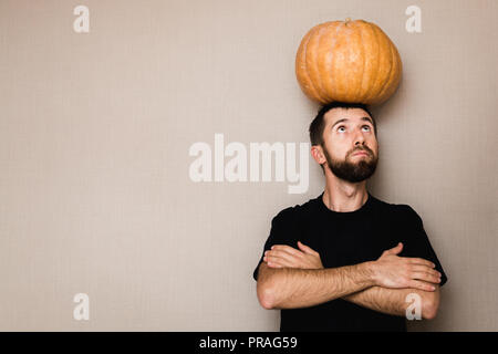 Junge bärtige Mann in Schwarz t-shirt kleine Kürbis über seinem Kopf Stockfoto