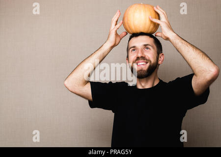 Junge lächelnde bärtigen Mann in schwarzen T-Shirt kleine Kürbis über seinem Kopf Stockfoto