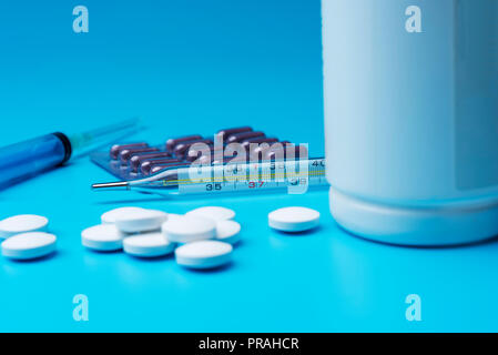 Weiße Pillen auf einem blauen Hintergrund und eine offene Flasche zerstreut. Nahaufnahme, Medikamente. Stockfoto