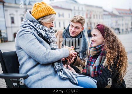 Zwei Jugendliche, die eine Gegenwart in eine Großmutter im Rollstuhl im Freien im Winter. Stockfoto