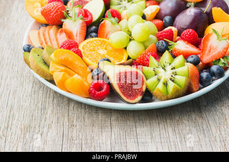 Gesundes Obst und Beeren Platter, Pflaumen Erdbeeren Himbeeren Orangen, Äpfel, Kiwis, Weintrauben, Heidelbeeren auf grau Holztisch, Nahaufnahme, kopieren Raum Stockfoto