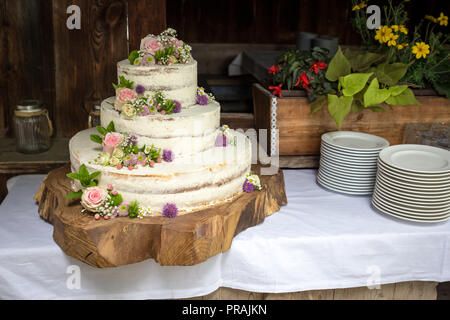 Weisse Hochzeitstorte mit Rosen und Blumen auf einem Baum. Stockfoto