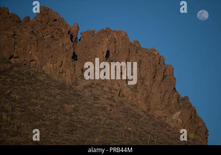 Vollmond, Sonnenaufgang Blick über die orange farbigen Felsen und spärliche Wüstenvegetation in San Carlos, Sonora, Mexiko. Luna Llena, Vista al Amanecer Stockfoto