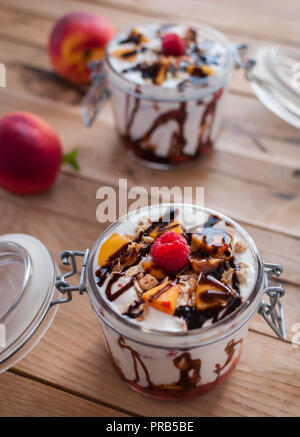 Close-up von Peach Parfait mit Joghurt, Müsli und Schokolade in einem Glas nachfüllen Stockfoto