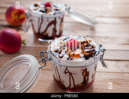 Close-up von Peach Parfait mit Joghurt, Müsli und Schokolade in einem Glas nachfüllen Stockfoto