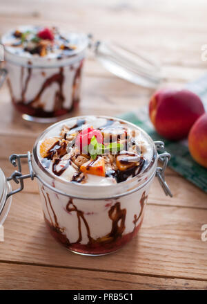 Close-up von Peach Parfait mit Joghurt, Müsli und Schokolade in einem Glas nachfüllen Stockfoto