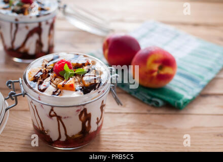 Close-up von Peach Parfait mit Joghurt, Müsli und Schokolade in einem Glas nachfüllen Stockfoto