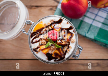 Close-up von Peach Parfait mit Joghurt, Müsli und Schokolade topping in einem Glas, Ansicht von oben Stockfoto