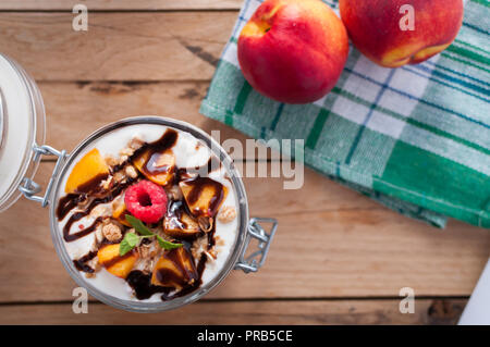 Close-up von Peach Parfait mit Joghurt, Müsli und Schokolade topping in einem Glas, Ansicht von oben Stockfoto
