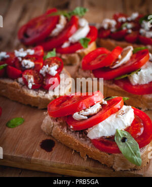 Bruschetta mit Käse, Tomaten, frischem Basilikum und Balsamico Essig auf Schneidebrett Stockfoto