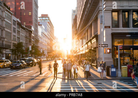 NEW YORK CITY, ca. 2018: Helles Licht der untergehenden Sonne scheint auf Massen von Menschen überqueren die Kreuzung auf der 5th Avenue in Manhattan, New York City Stockfoto