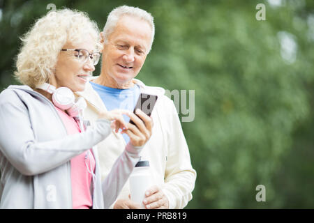 Im Alter von Frauen, die ihren Mann etwas in Smartphone nach Outdoor Training Stockfoto