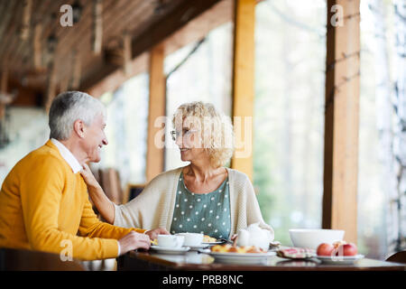 Gerne schöne ältere Frau mit lockigem Haar Brille Berühren der Schulter der Mann und ihn unterstützen, während Sie sprechen beim Frühstück auf der Veranda Stockfoto