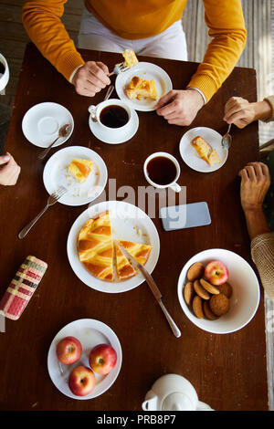Hohe Betrachtungswinkel der unkenntlich senior Freunde an den hölzernen Tisch und trinken schwarzen Tee mit Kuchen, Kekse und Äpfel sitzen Stockfoto
