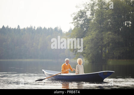 Aufgeregt gut aussehender älterer Freund in gelb Pullover sitzen auf dem Boot mit geliebte Frau und Rudern Rudern am Tag auf See Stockfoto