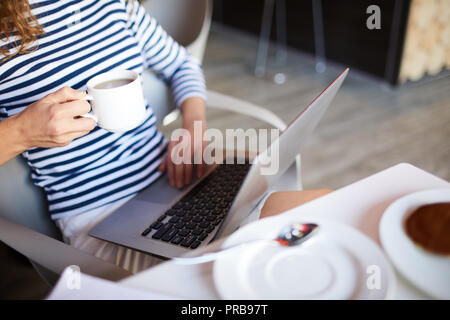 Nahaufnahme der unkenntlich Frau in abgestreift Pullover mit Laptop und trinken Kaffee in der modernen Cafe mit Wlan Stockfoto