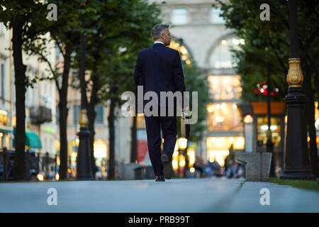 Rückansicht der elegante Mann im Anzug mit Aktentasche und Mantel Central Street hinunter. Stockfoto