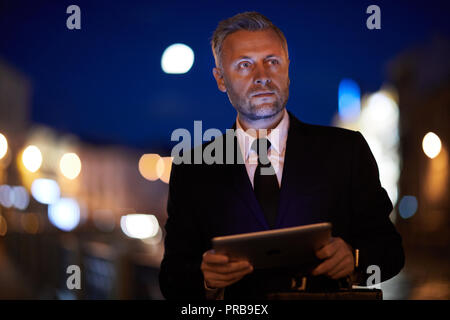 Ernsthafte junge Unternehmer mit Tablet Chillen am Abend Stockfoto