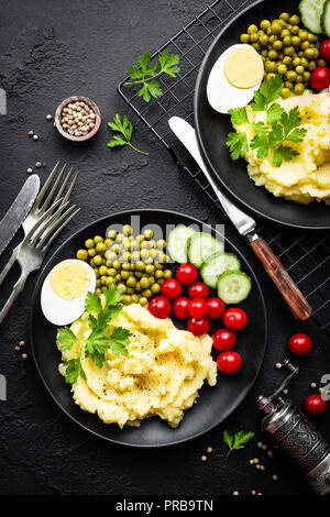 Kartoffelpüree mit grünen Erbsen, Tomaten, Gurken und gekochtem Ei. Kartoffelschnee auf Platte mit Gemüse und Ei Stockfoto