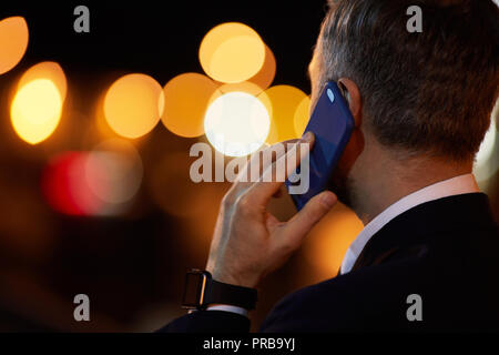 Junge elegante Geschäftsmann sprechen von Smartphone auf Schaumwein Hintergrund bei Nacht Stockfoto