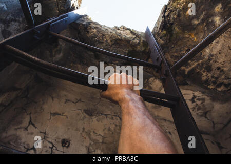 Rostiges Metall Leiter mit männlichen Hand it Holding, leeren dunklen Turm Innenraum mit glühenden Ende Stockfoto