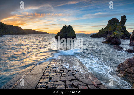 Dramatischer Sonnenuntergang über dem Meer Stacks und ein alter Stein Mole in Pettico Wick Bay in St. Abbs in den Scottish Borders Stockfoto