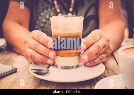 Nahaufnahmen der Hände mit transparentem Glas Kaffee und hölzernen Tisch Stockfoto