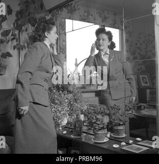Frau in den 1950er Jahren. Eine junge braunhaarige Frau steht vor einem Spiegel an der Wand, ihr Make-up-Kontrolle. Sie trägt eine Jacke und Rock in der gleichen Stoff Material. Bilder Schauspielerin Marion Sundh, 1927-1987, hom 1951. Ref 1689 Stockfoto