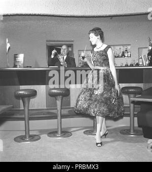 Frau in den 1950er Jahren. Eine junge Frau steht in einer Bar mit einem Drink in der Hand. Sie trägt ein schickes Kleid mit Blumen. Schweden 1956. Foto Kristoffersson Ref von 71-5 Stockfoto