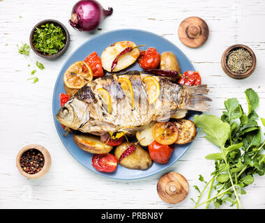 Gegrillter Fisch mit Bratkartoffeln und Gemüse auf dem Teller Stockfoto