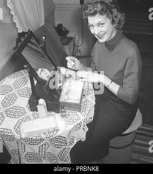 Make-up in den 1950er. Eine junge Brünette lackiert ihre Nägel. Sie hat einen praktischen Spiegel und eine Make-up-Box auf dem Tisch vor sich. Schweden 1954. Foto Kristoffersson Ref. BO47-1 Stockfoto