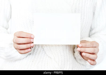 Nahaufnahme der Frau Hände in Weiß Strickpullover Holding leeres Papier Karte. Grußkarte Mock-up. Chritsmas winter Design. Feminin Foto. Stockfoto