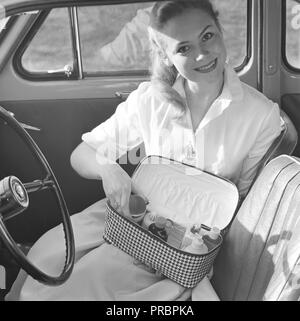 Make-up in den 1950er Jahren. Eine junge blonde Frau in einem Auto zeigt ihr praktisches Make-up-Tasche mit Parfums, Cremes und Kosmetika. Schweden 1957 Stockfoto