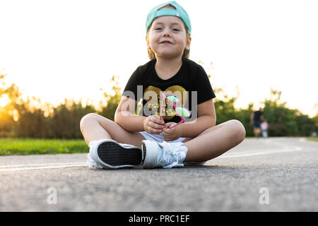 Mode Mädchen Kind trägt eine Kappe und T-Shirt in der Stadt sitzen. Stockfoto