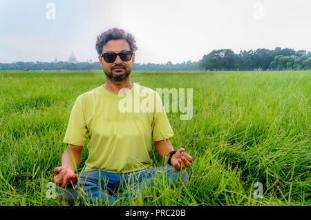 Yoga im Park. Älterer bärtiger Mann im Lotussitz sitzen auf grünem Gras. Konzept der Ruhe und Meditation. junger Mann in Sonnenbrille meditieren im Freien in t Stockfoto