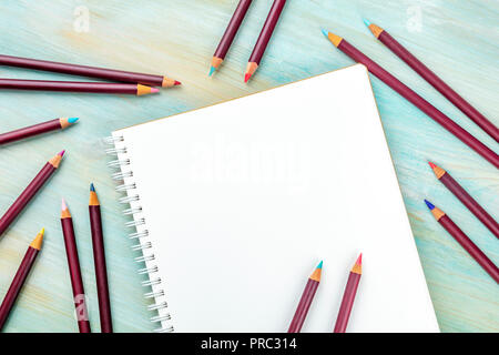 Ein Foto von einem shetchbook mit vielen verschiedenen Farbstifte um ihn herum, geschossen von oben auf eine blaugrüne Hintergrund mit Kopie Raum Stockfoto
