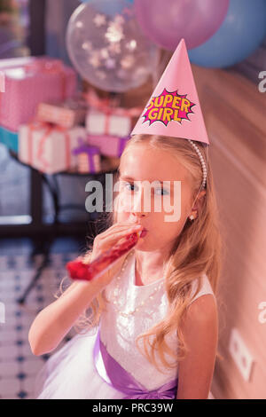 Lustig Mädchen bläst ihre Partei Horn und Suchen nette Stockfoto