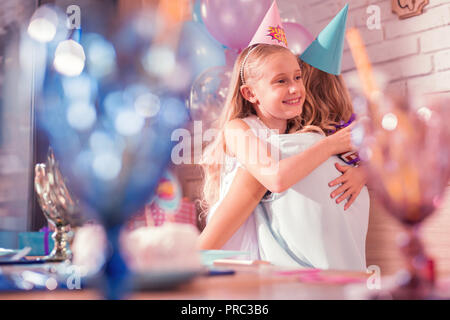 Süße blonde Mädchen ihre Mutter umarmt und suchen gerne an der Partei Stockfoto