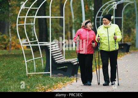 Reife Frauen sind im skandinavischen Wandern im Herbst im Park, neben der Sitzbank Stockfoto