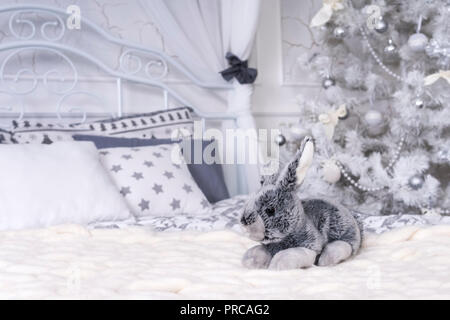Spielzeug Kaninchen in ein Bett auf einer Plaid mit einem Weihnachtsbaum im Hintergrund Stockfoto